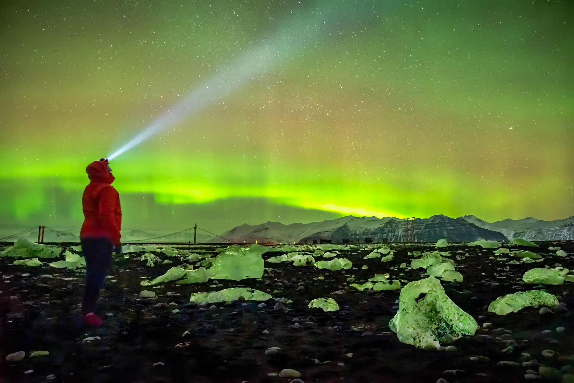 Person watching aurora borealis during strong bright green and red northern lights display in unique amazing travel experience. Diamond beach, Iceland
